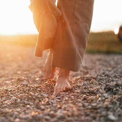 Close up of womans barefoot feet walking on a rock beach.