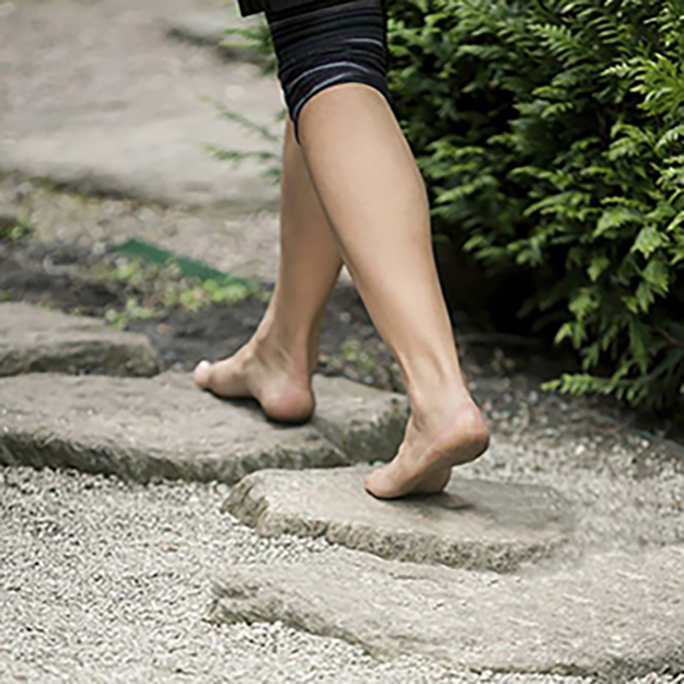 A woman walking down the stepping stones in a zen-like japanese garden.