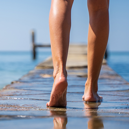 Legs of a girl walking on a wooden bridge in the middle of the ocean moving away towards the horizon in the sea